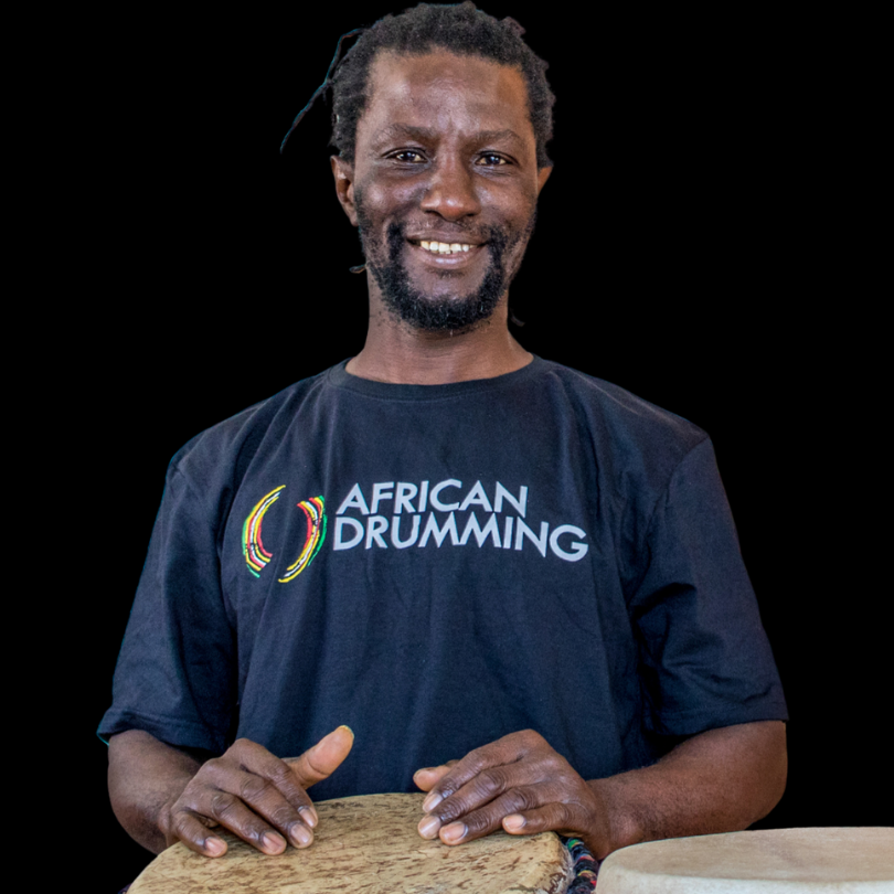 Yaw, nz drum camp teacher, smiling and playing the djembe