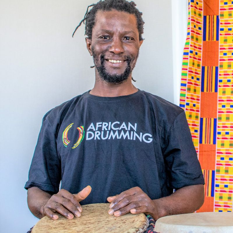 Yaw, nz drum camp teacher, smiling and playing the djembe